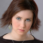 Attractive young woman with brown hair and stylish haircut; making direct eye contact with viewer